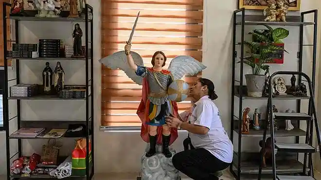 A woman cleans a statue of a saint displayed beside books on exorcism at the Saint Michael Center for Spiritual Liberation and Exorcism in Makati, Metro Manila, Philippines.